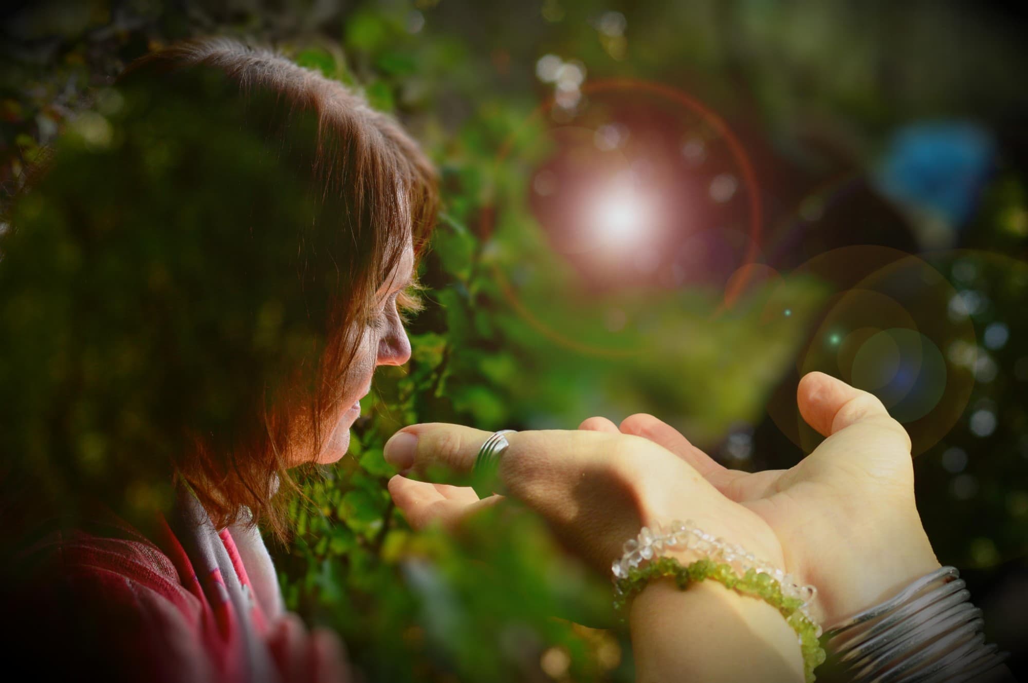 A woman holding light in cupped hands in a green setting